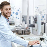 Computer at the lab. Young man working at the medical laboratory using computer to operate analyzing machines copyspace modern technology research science chemistry pharmaceutical medicine job concept