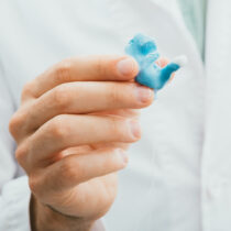 Doctor holding in his hands molded individual hearing aid earmolds for his patient, close-up. Hearing solution